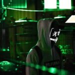 Person in a hooded mask with green glowing light, representing what happens during a cybersecurity incident and how organizations respond to a breach.